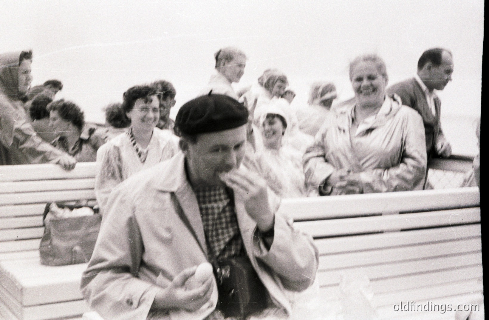 A group of people, likely tourists, are seated on a boat's deck. A man in a beret and light jacket appears central, holding a small object. Several women with 1950s hairstyles are visible. The scene suggests a seaside excursion. Likely mid-20th century. Stock potential for vintage travel & leisure themes.