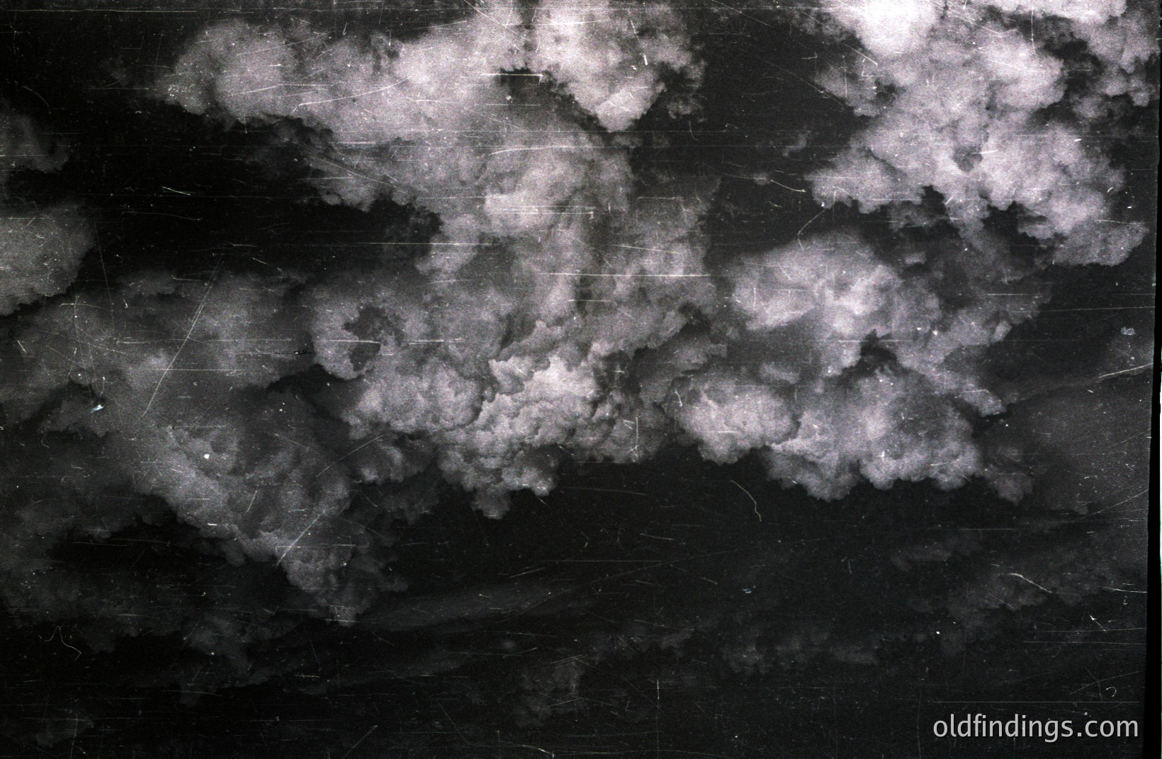 Striking black and white photograph depicting a dramatic, turbulent cloudscape. High contrast reveals textured cloud formations against a dark sky. Visible scratches & marks suggest age/archival origin, possibly a vintage atmospheric study or meteorological documentation.