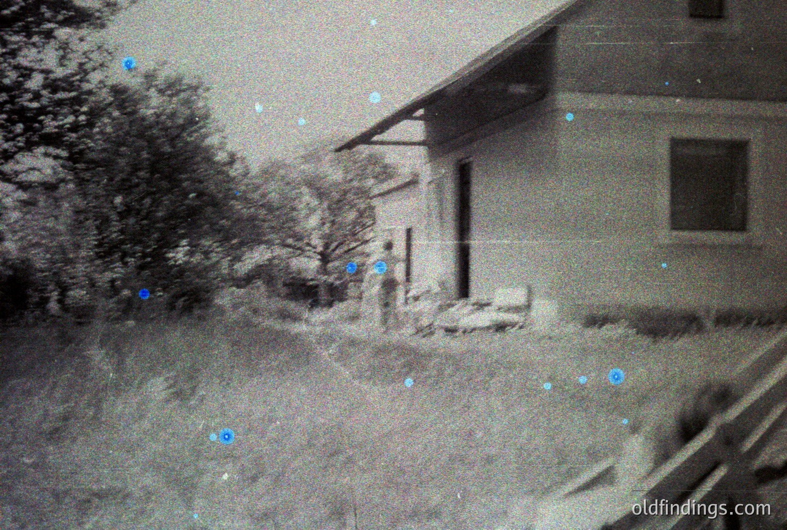 A grainy, black-and-white photograph captures a simple, single-story building with a low-pitched roof and a visible window. The structure appears to be surrounded by overgrown vegetation and a grassy area. Likely taken mid-century, possibly the 1950s or 60s. Could be a rural home or outbuilding. Offers potential for design reference.