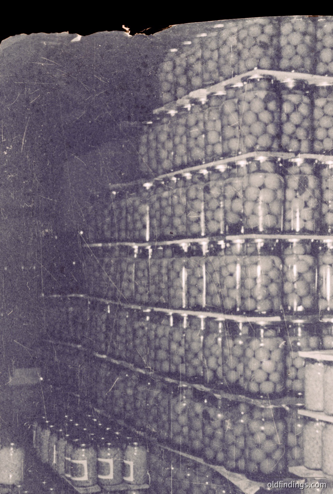 Stacked shelves are laden with round jars, likely preserved food, suggesting a pantry or industrial storage. The grayscale tones & visible scratches indicate an aged photograph, possibly dating to the mid-20th century. A strong architectural composition, this image could be valuable for design references or historical food preservation research.