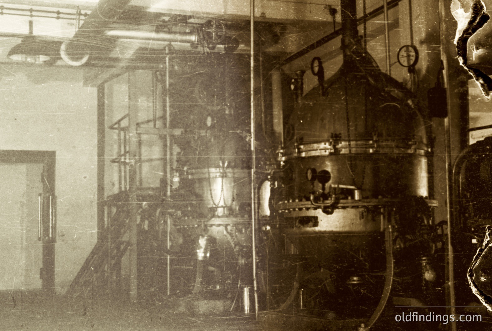 Industrial interior featuring large, complex machinery—likely processing or refining equipment. Visible piping, gauges, and metal structures suggest a factory or laboratory setting, possibly early 20th century. The photograph’s aged appearance, with scratches and tonal variation, adds to its historical character.