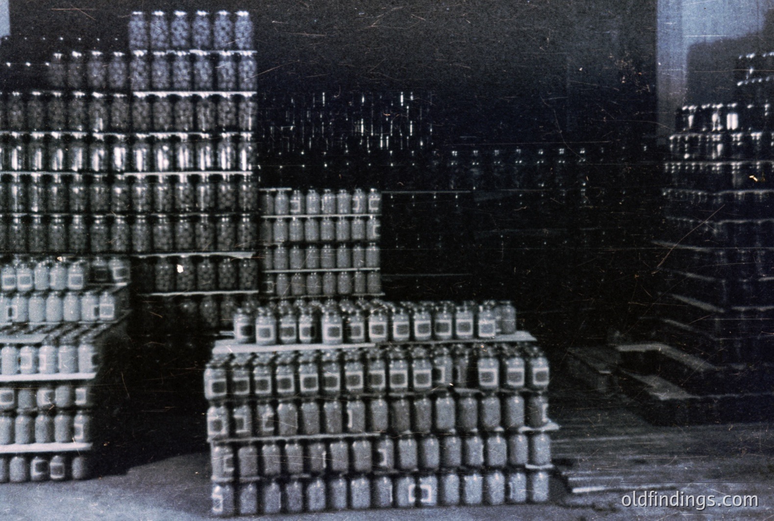 Stacked crates filled with clear glass bottles dominate this black and white photo, likely a warehouse or bottling facility. The repetitive pattern suggests mass production, possibly beverages or pharmaceuticals. Appears to be mid-20th Century industrial documentation. Simple composition, suitable for commercial use.