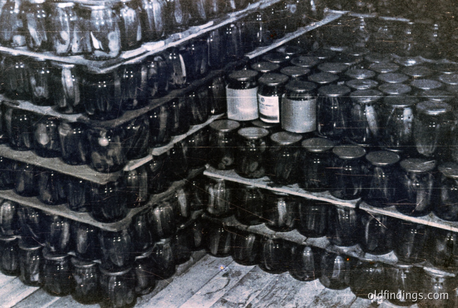 Massive shelving unit densely packed with glass jars, possibly preserves or canning goods. Black and white photo suggests a period warehouse or industrial storage space, likely mid-20th century. A single, unlabeled jar sits prominently near the front. Strong composition, evokes a sense of abundance.