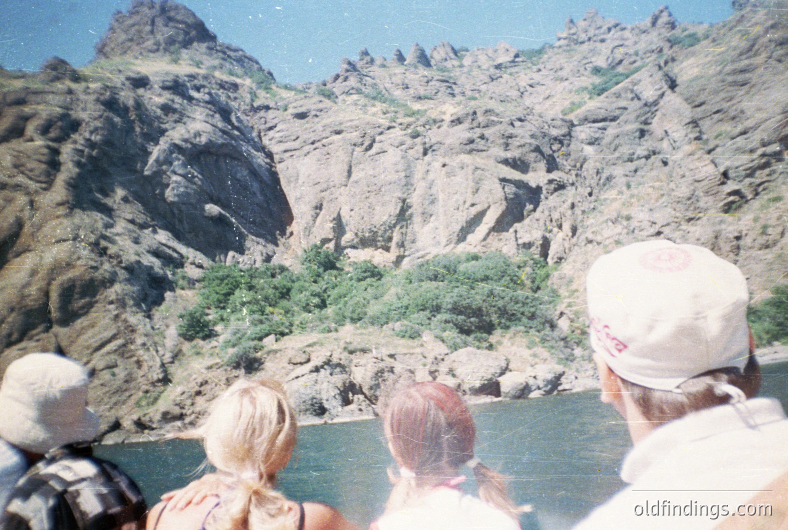Family observes towering rock formations from a boat on a river, likely during a recreational outing. The eroded, layered cliffs show geological strata. Color palette suggests a warm, sunny day, possibly 1970s era based on film quality and style. Potential stock photography reference.