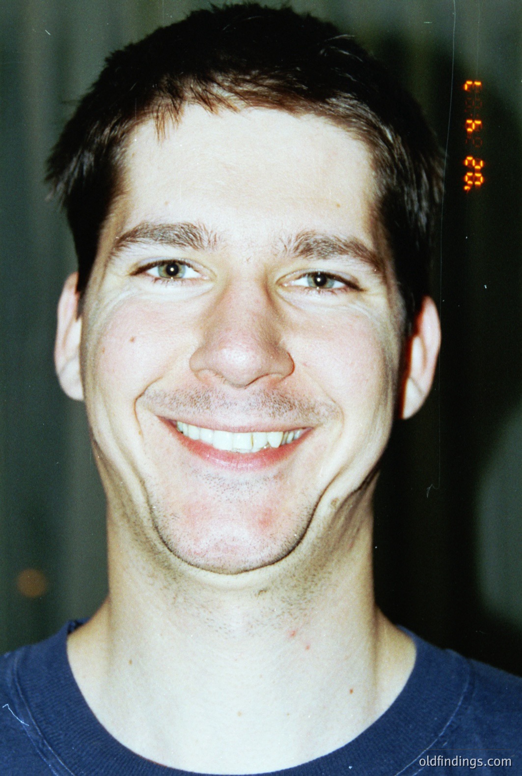 Close-up portrait of a young man smiling broadly. Short, dark hair and fair skin. Appears to be wearing a blue crew neck shirt. The image has a dated, slightly grainy quality suggestive of film photography, possibly the late 1990s or early 2000s. Date visible at upper right.