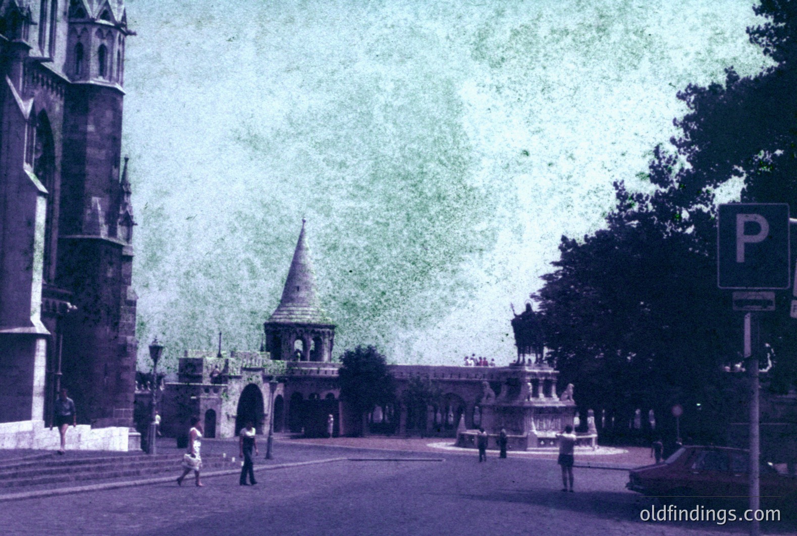 A color photo shows a wide plaza with a monumental archway. The architecture suggests a European seaside city, likely Bulgaria’s Varna. A fountain stands beneath the arch, flanked by pedestrian walkways. A vintage car and pedestrians are visible. Likely 1970s.