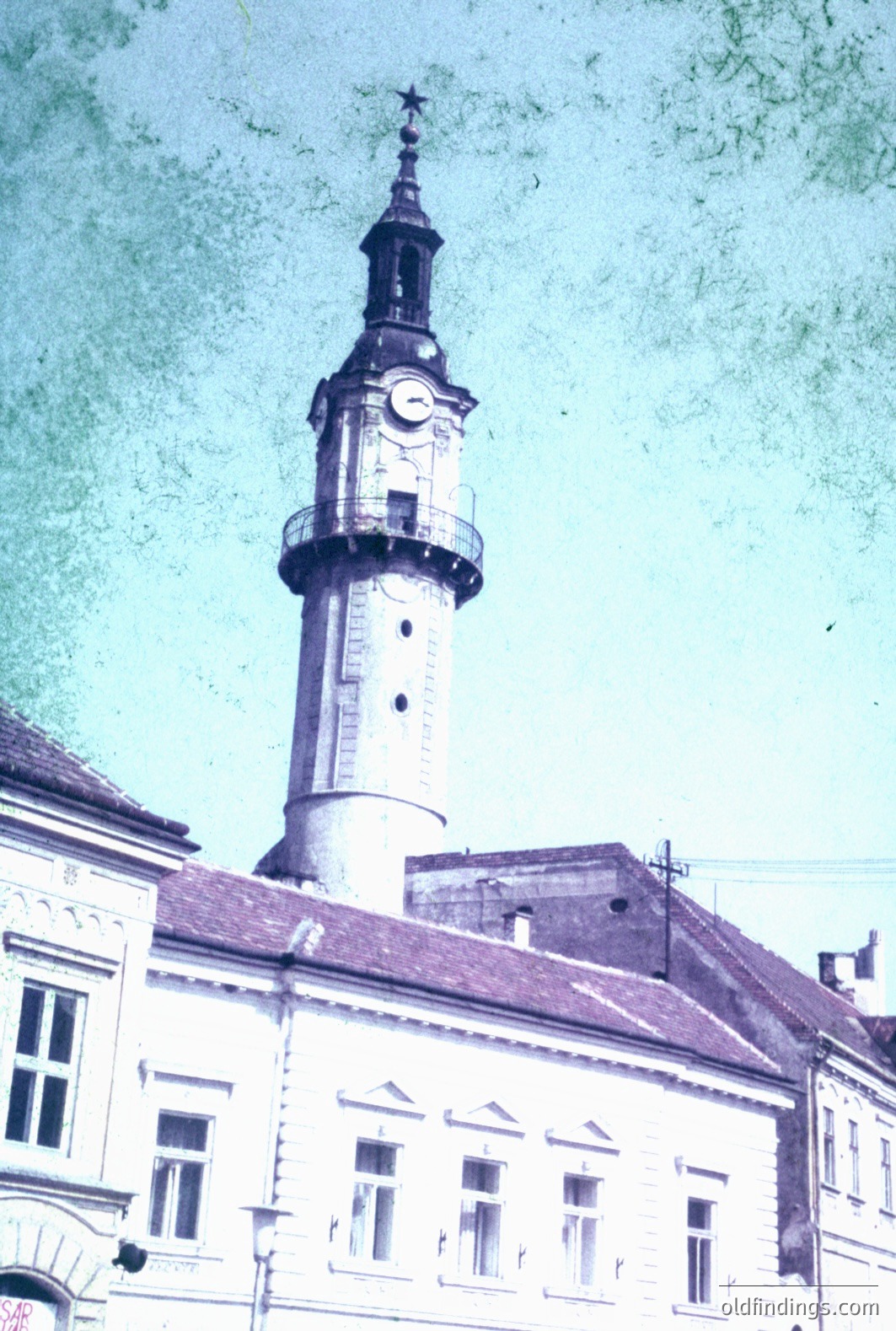 This color photograph shows a stately building topped by a tall clock tower, likely a municipal structure. The architecture features classical detailing and a distinctive, tiered clock tower with a spire and star. The image shows signs of age and discoloration. Likely taken in Eastern Europe.