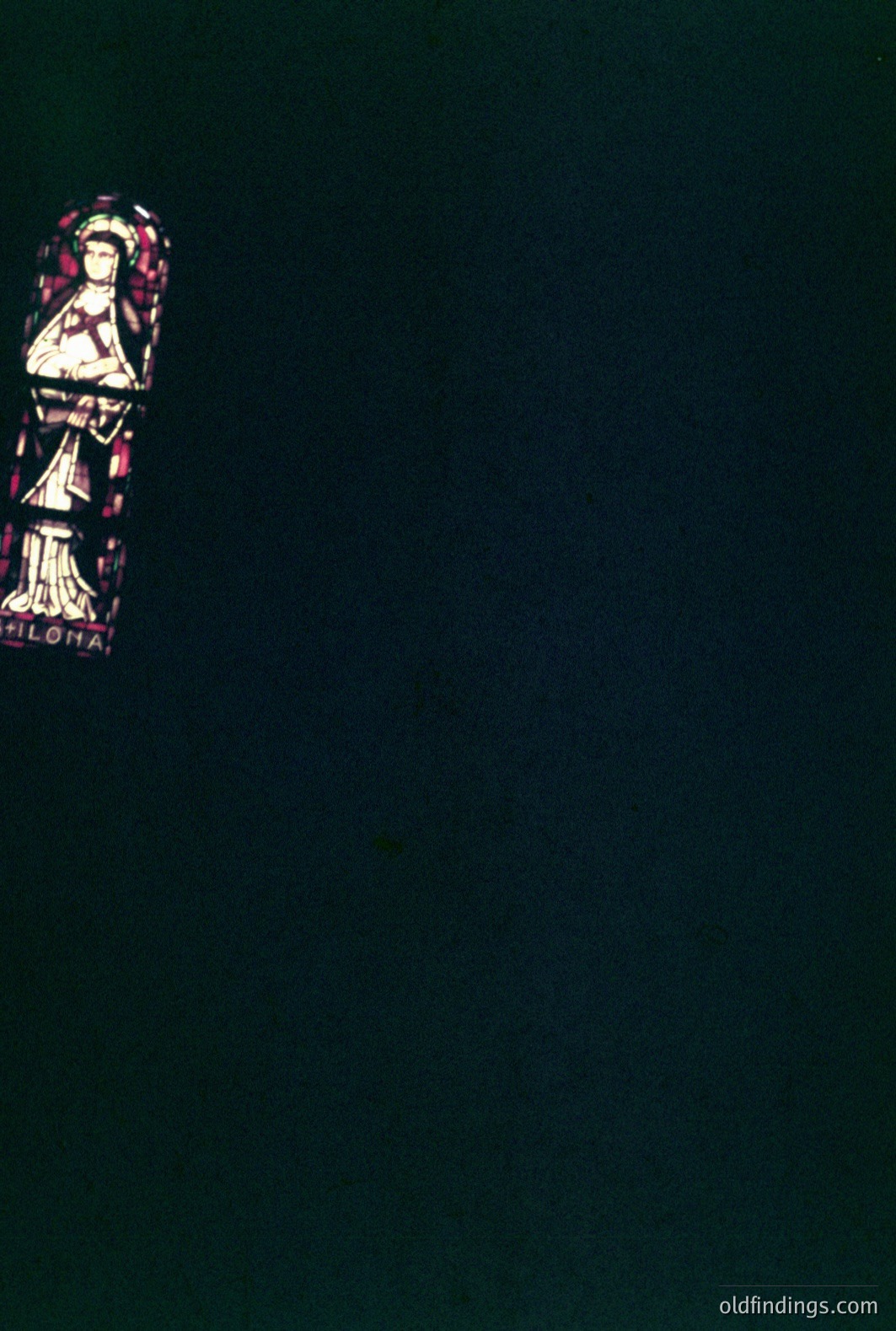 Fragment of a stained-glass window featuring a robed figure, likely a saint, depicted in profile. Vibrant blues, reds, and greens comprise the design. Likely a religious context, potentially ecclesiastical architecture. Late 19th/early 20th century stylistic elements. Visible inscription partially reads "SILOHA".