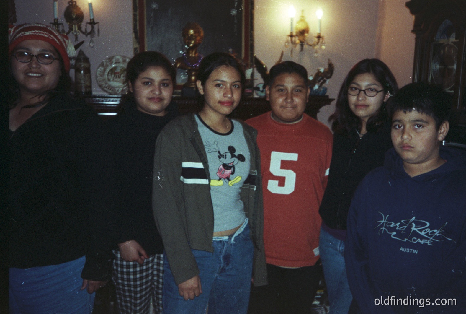 Group portrait of six young people, likely family members, standing indoors. Visible background details include a chandelier, mirrors, and ornate woodwork. Clothing suggests a casual, late 1990s/early 2000s style. Potential stock photo for family themes.
