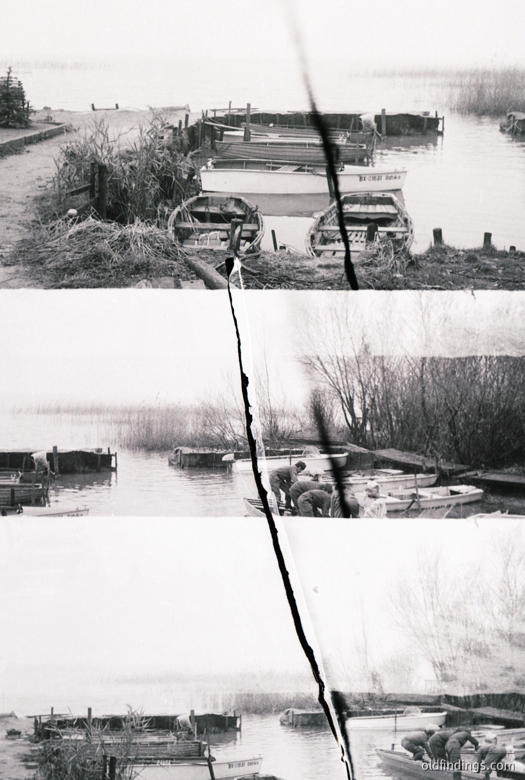 A b&w photo showcases a quiet lakeside scene, featuring rowboats docked along a weathered wooden pier. Shoreline vegetation and distant trees frame the water. Three men in military attire are present, observing the boats. Likely a military training exercise or reconnaissance. Appears mid-20th century.