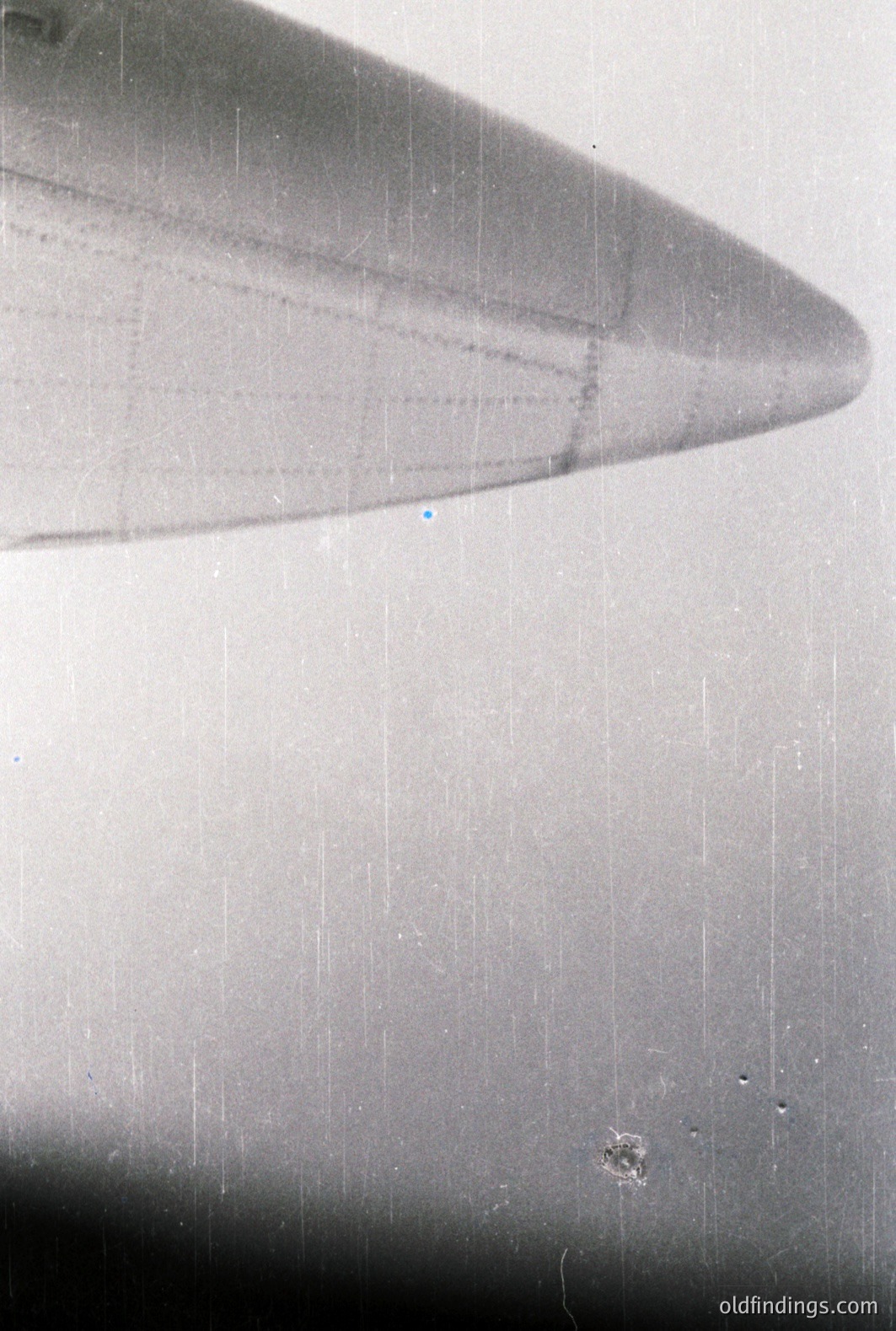 A grayscale, high-angle view focusing on the wing of an aircraft, partially visible. The image exhibits significant dust and scratch artifacts consistent with aged photographic materials. Likely a vintage document or press image. Commercial potential for archival research or texture design.