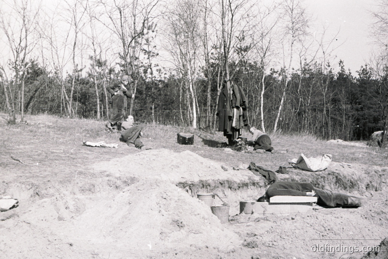 Archaeological excavation in progress. Visible are several workers carefully uncovering skeletal remains within a sandy, sloped site. Tools, buckets, and measuring devices are present. Appears to be a large-scale dig with what may be a prehistoric burial. Likely 20th-century documentation.