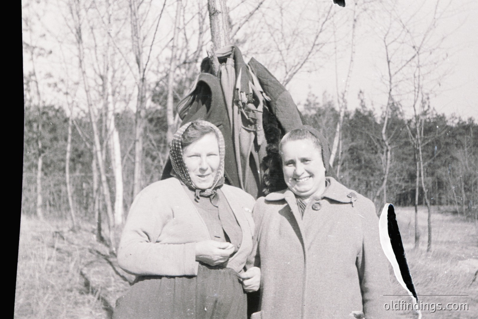 Two women in winter coats & headscarves pose outdoors, likely in a rural setting. Appears to be a candid portrait, possibly a family snapshot. Simple attire & backdrop suggest a mid-20th century, possibly 1950s-1970s, origin. Good reference for historical costuming or group portraiture.