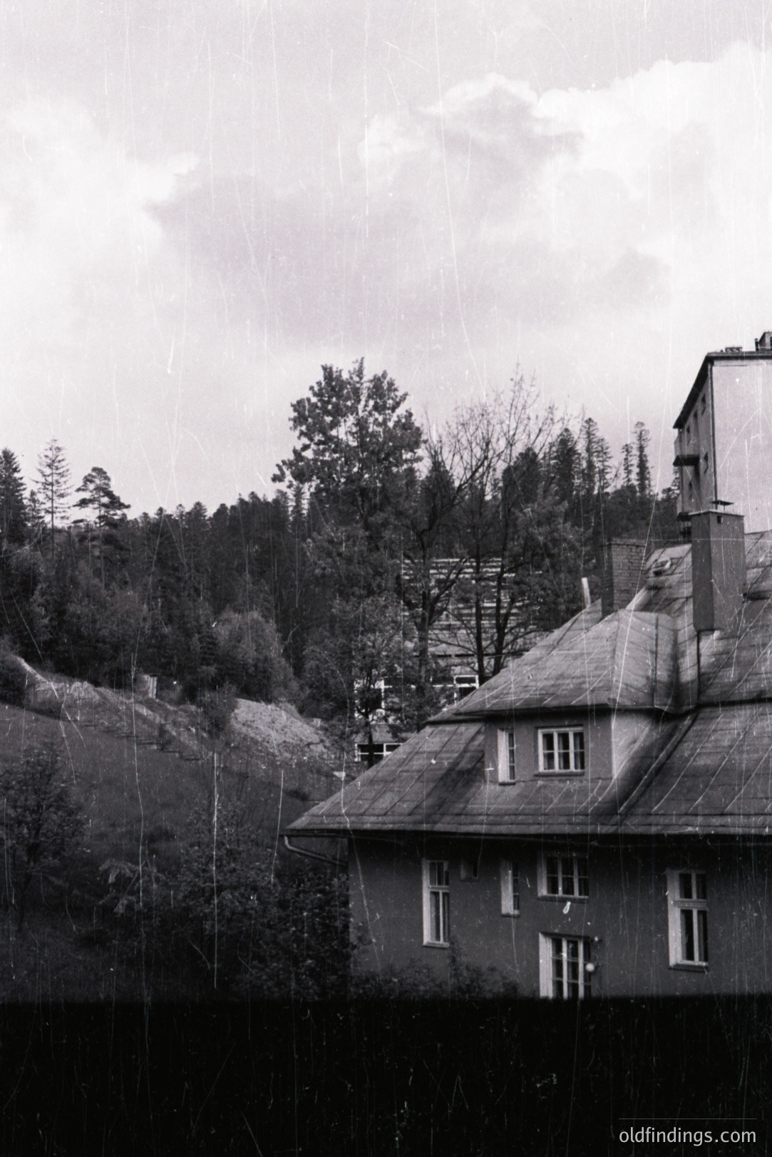 Charming, slate-roofed villa ascends a wooded hillside. Likely residential, the structure features multiple windows, decorative detailing, and a chimney stack. The aged photograph shows evident grain and surface wear. Possible Central European location, 1930s-1950s.