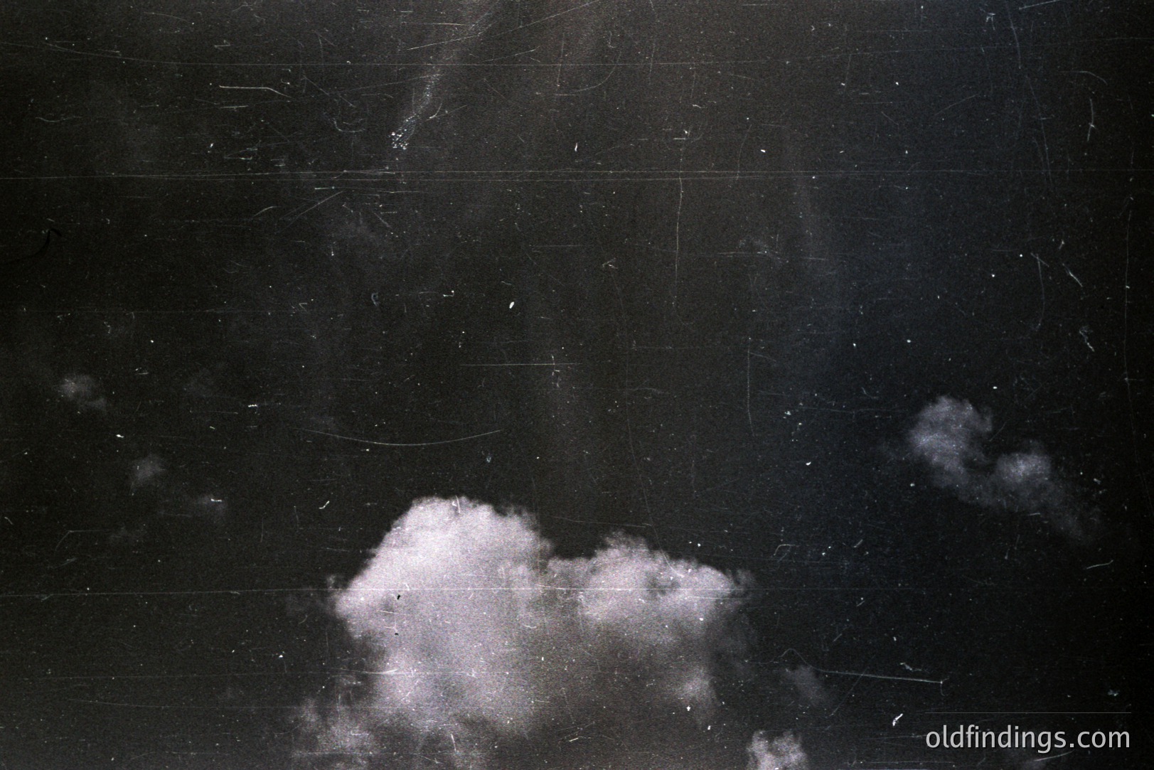 Striking black and white photograph showing clouds against a dark sky. Significant surface scratches and dust marks are visible, suggesting age and likely film origin. Evokes a vintage aesthetic, potentially from the mid-20th century or earlier. Ideal for design or texture overlays.