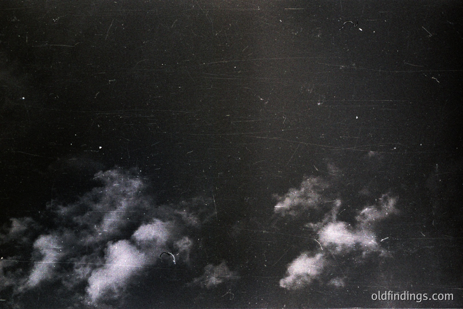 Strikingly textured black and white image depicting clouds at night. Visible scratches and marks across the surface suggest age and potential stock photo use for vintage effects. Atmospheric and moody, ideal for design or historical overlays. Likely 20th century production.