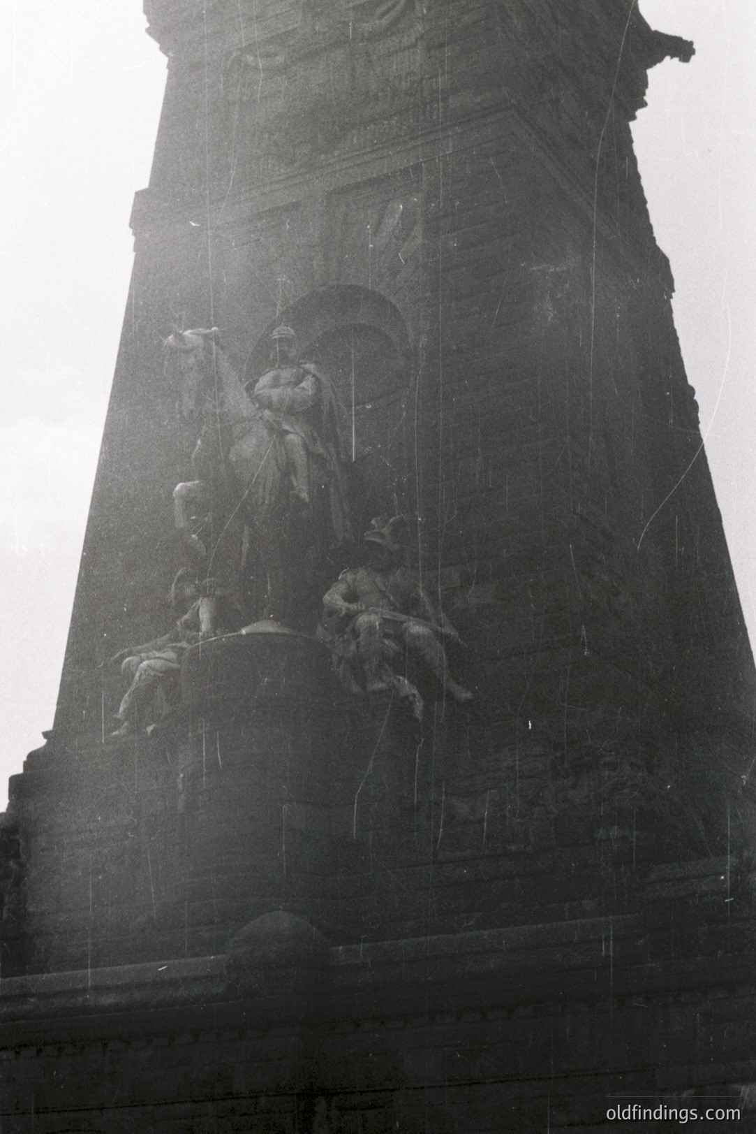 Close-up of a monumental stone sculpture depicting a seated, regal figure accompanied by allegorical figures. Part of a larger architectural structure, likely a memorial or palace façade. Appears to be a European style, possibly 19th century. Notable weathering & age apparent. Archival quality, showing surface wear.