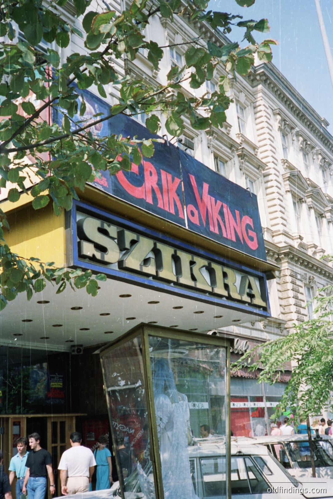 Ornate, three-story building facade displaying “VIKING” and "SZKRA" signage, likely a theater or cinema. Reflective storefront partially obscures street scene. Likely post-socialist era architecture, early 1990s or 1980s, Eastern Europe. Commercial value: vintage signage reference.