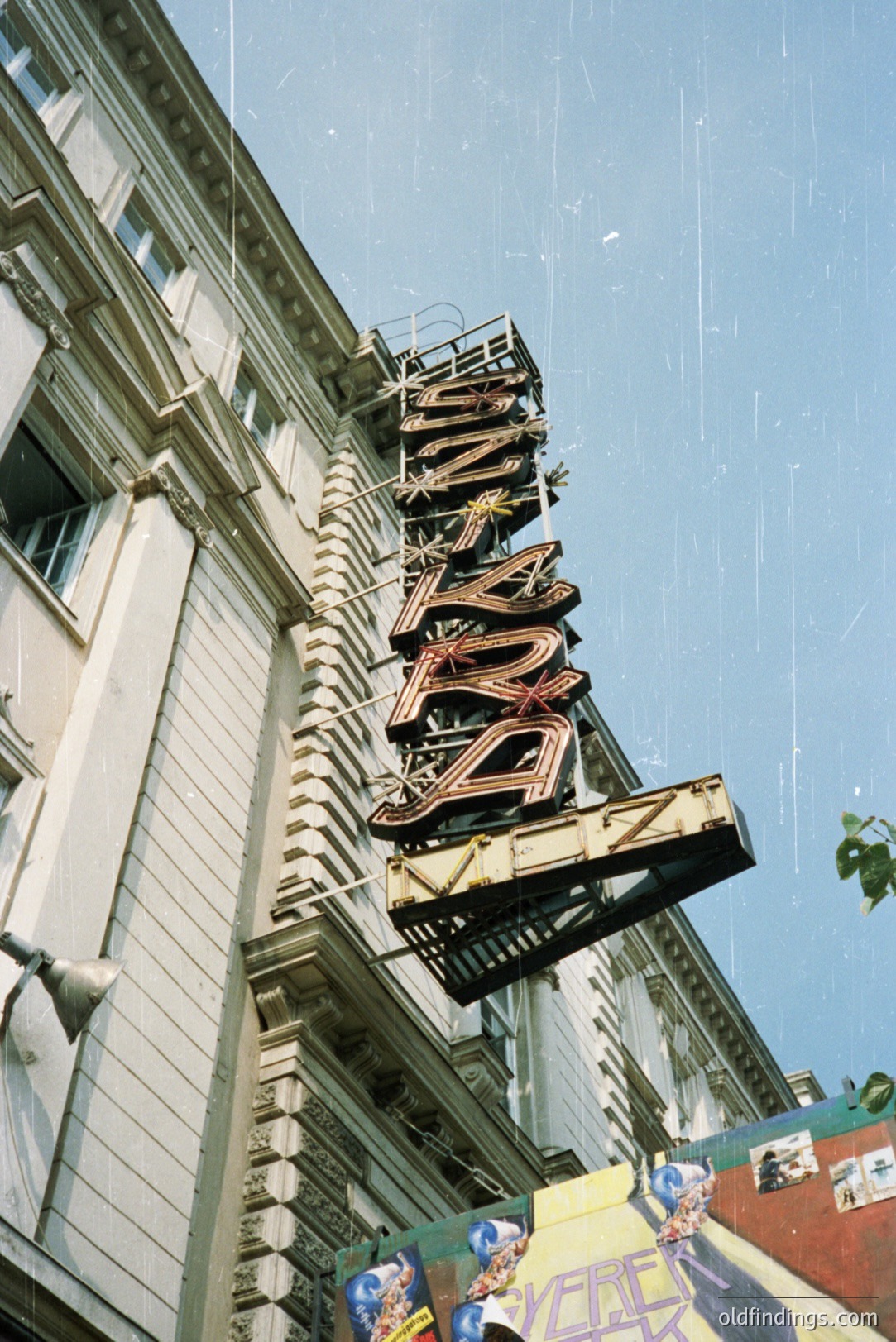 Striking, vintage neon sign proclaiming “Royal,” suspended from a formal, multi-story building with ornate window detailing. Likely a theater or entertainment venue. Visible aging and weathering suggest a period aesthetic. Appears to be a commercial district setting.