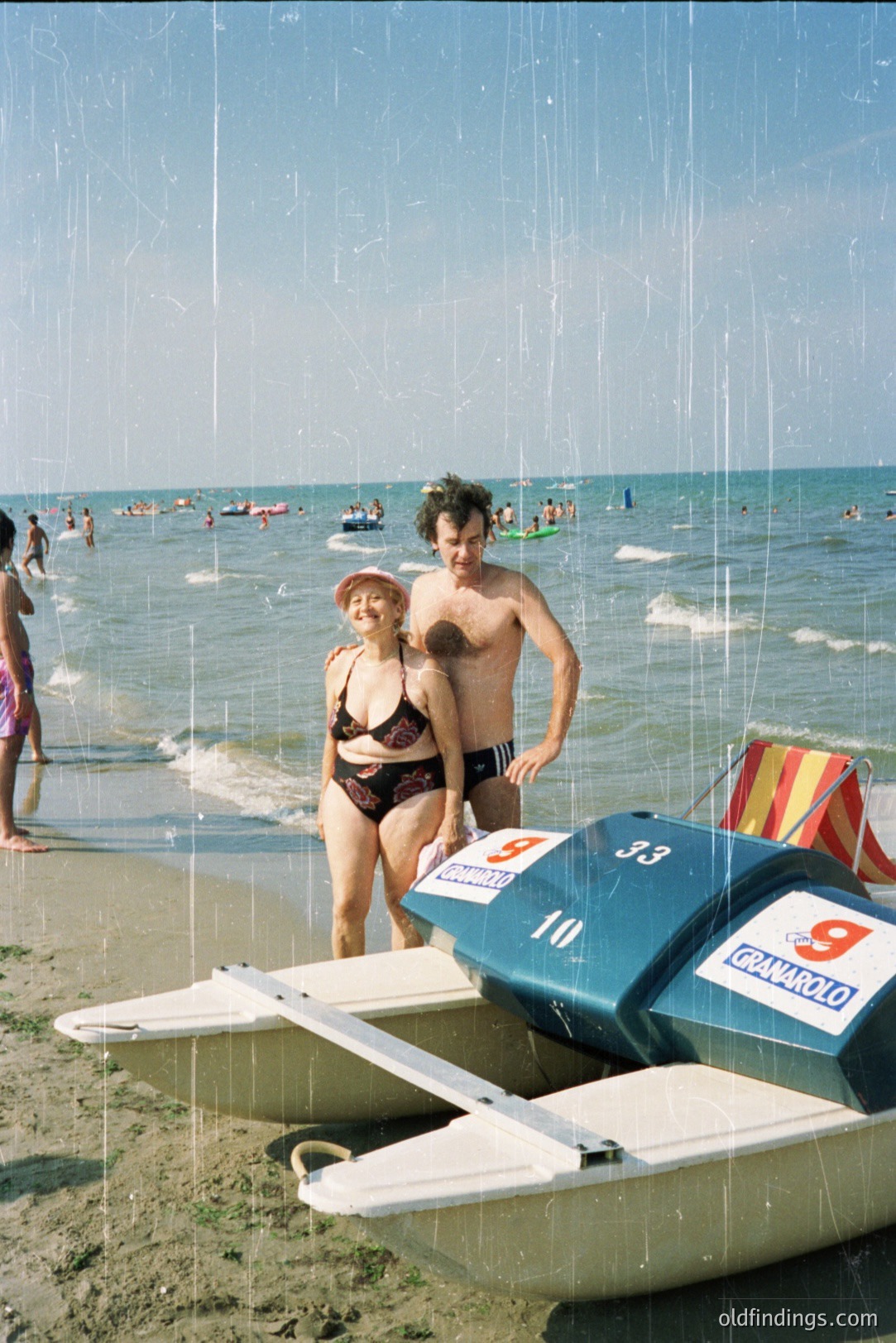A man and woman stand beside a numbered hydrofoil on a sandy beach; a crowd of bathers and boats fill the background. The “Granarolo” logo suggests a sponsorship or event. Likely coastal Bulgaria, 1970s or 80s. The visible film grain and color palette are characteristic of the era.