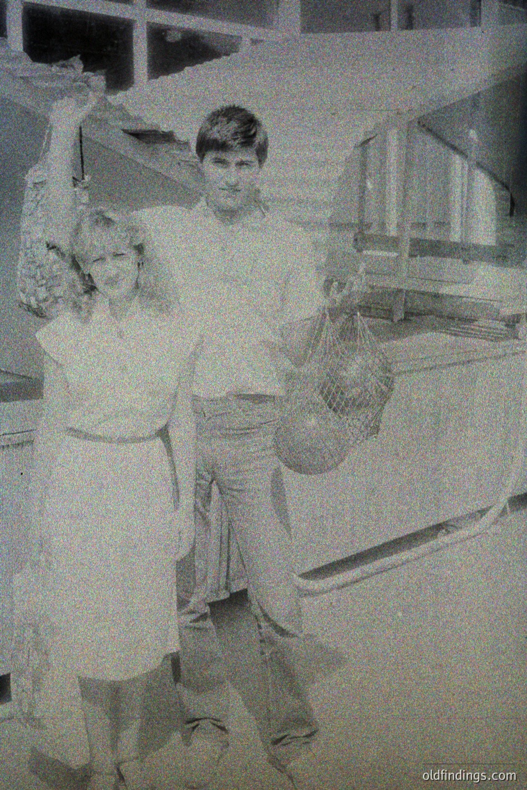 Young man and woman, likely fishermen, stand near a seafood display in what appears to be a market. She wears a short dress; he jeans and a simple shirt. The woven basket suggests a recent catch. Possible 1970s setting. Commercial use: vintage advertising, design reference.