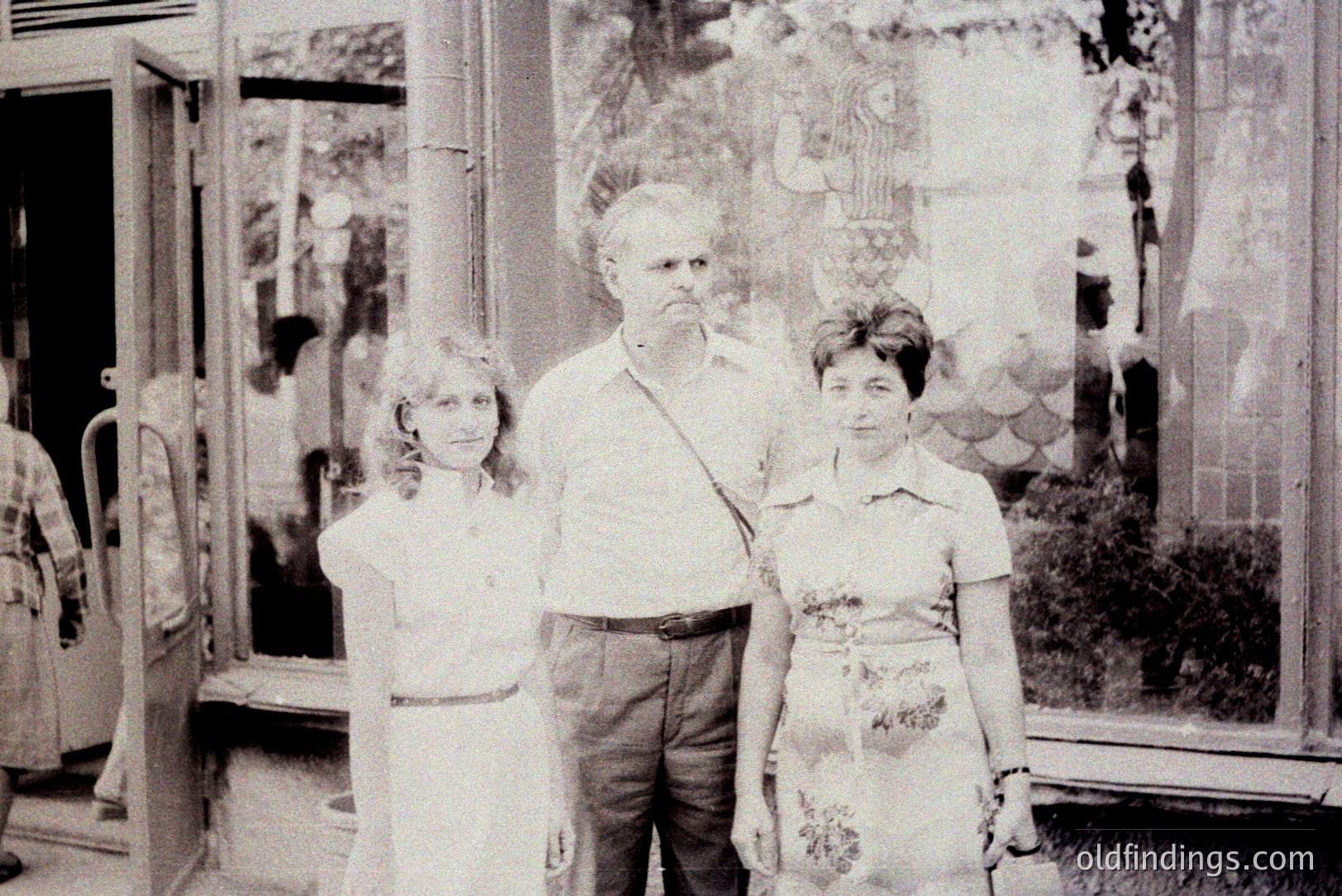 Formal portrait of a man flanked by two women, posed in front of a vibrant stained-glass window. Likely 1960s-70s, judging by clothing & photographic style. The window depicts a religious scene, adding cultural context. Appealing for design or historical reference.