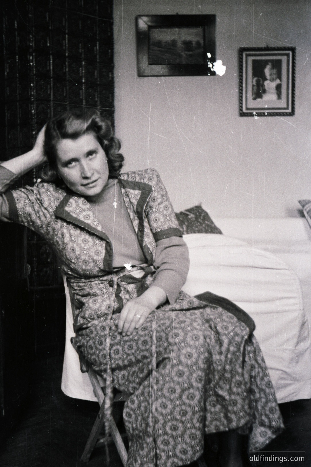 Vintage black and white portrait of a woman seated in a patterned dress. Detailed, decorative tilework adorns the background walls. A framed landscape and portrait hang above a bed. Likely mid-20th century domestic interior. May be of commercial stock photography interest.