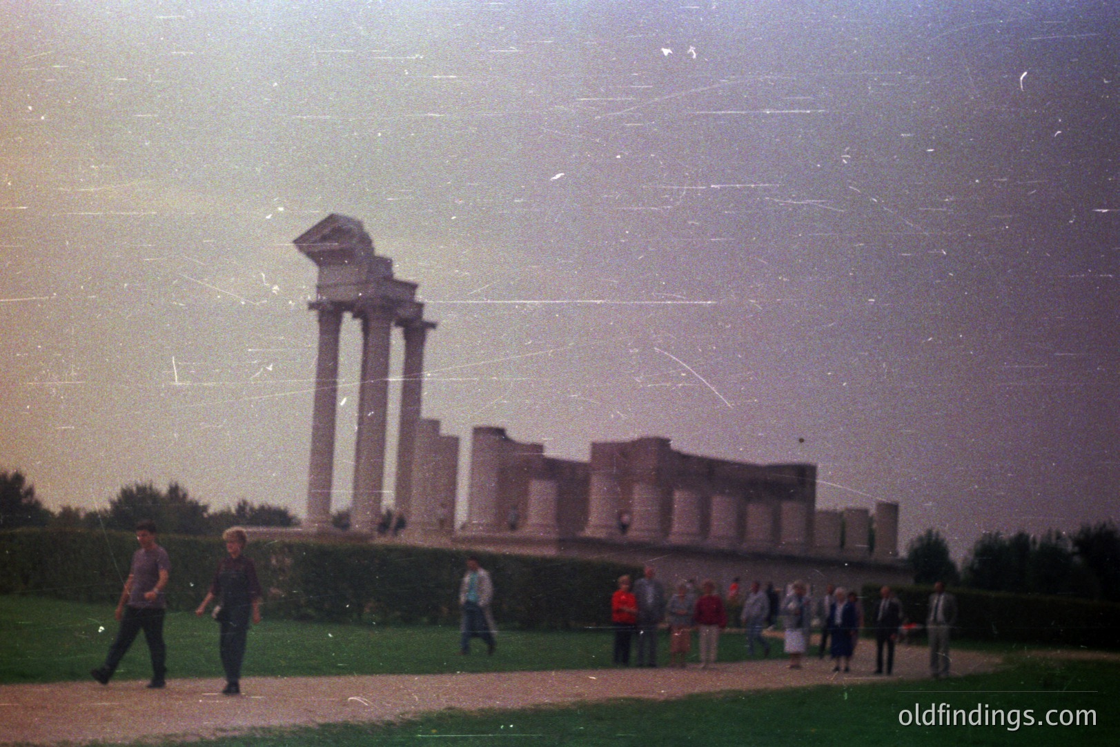 Striking view of the Roman ruins of Novae, Bulgaria. Remains of a provincial palace showcase impressive column architecture, with a small group of tourists exploring. Likely a 1970s-80s tourist snapshot, exhibiting film grain & color shifts. A detailed record of a historical site.