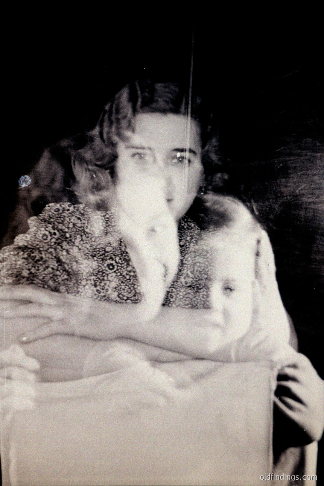 A striking, ghostly image: a woman in a beaded dress holds a child, both blurred by movement. The portrait evokes experimental photography of the early 20th century, likely 1920s-1930s. Subject's hairstyle and dress indicate a period of Art Deco influence. Commercial potential for design and vintage aesthetic studies.