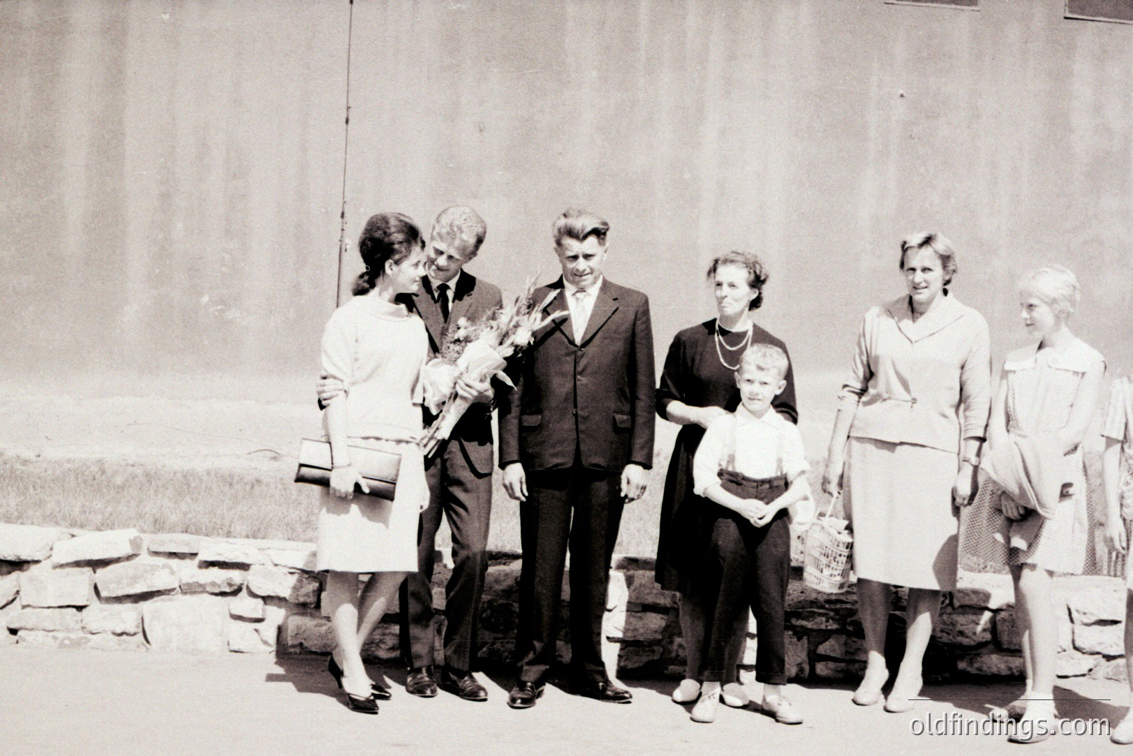 Formal portrait of a family of six, likely celebrating an event. The men wear dark suits and ties, the women modest dresses/skirts. Architectural background suggests a public building or institution. Appears to be from the 1960s or 1970s. Strong potential for historical or genealogical research.