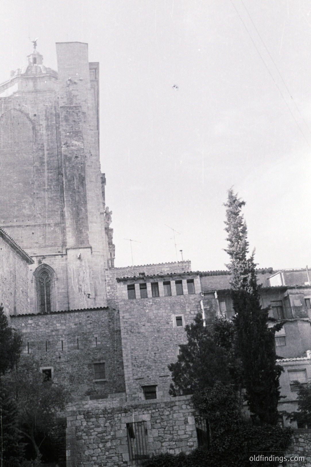 A tall, imposing stone church tower dominates this view, exhibiting Gothic architectural details. Adjacent structures show a mix of residential and commercial stonework. Appears to be a European coastal town, likely early to mid 20th century. Possible stock photo reference for historical architecture.