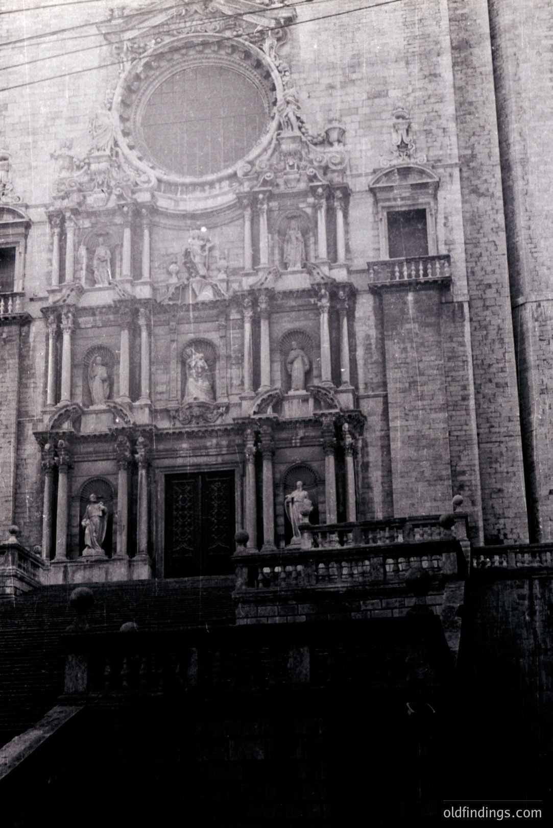 Ornate facade of a baroque-style building featuring sculptural relief, statues, and arched doorways. Monumental scale with a central circular window. Likely European origin, potentially 18th century. Architectural detail suitable for design references & historical research.