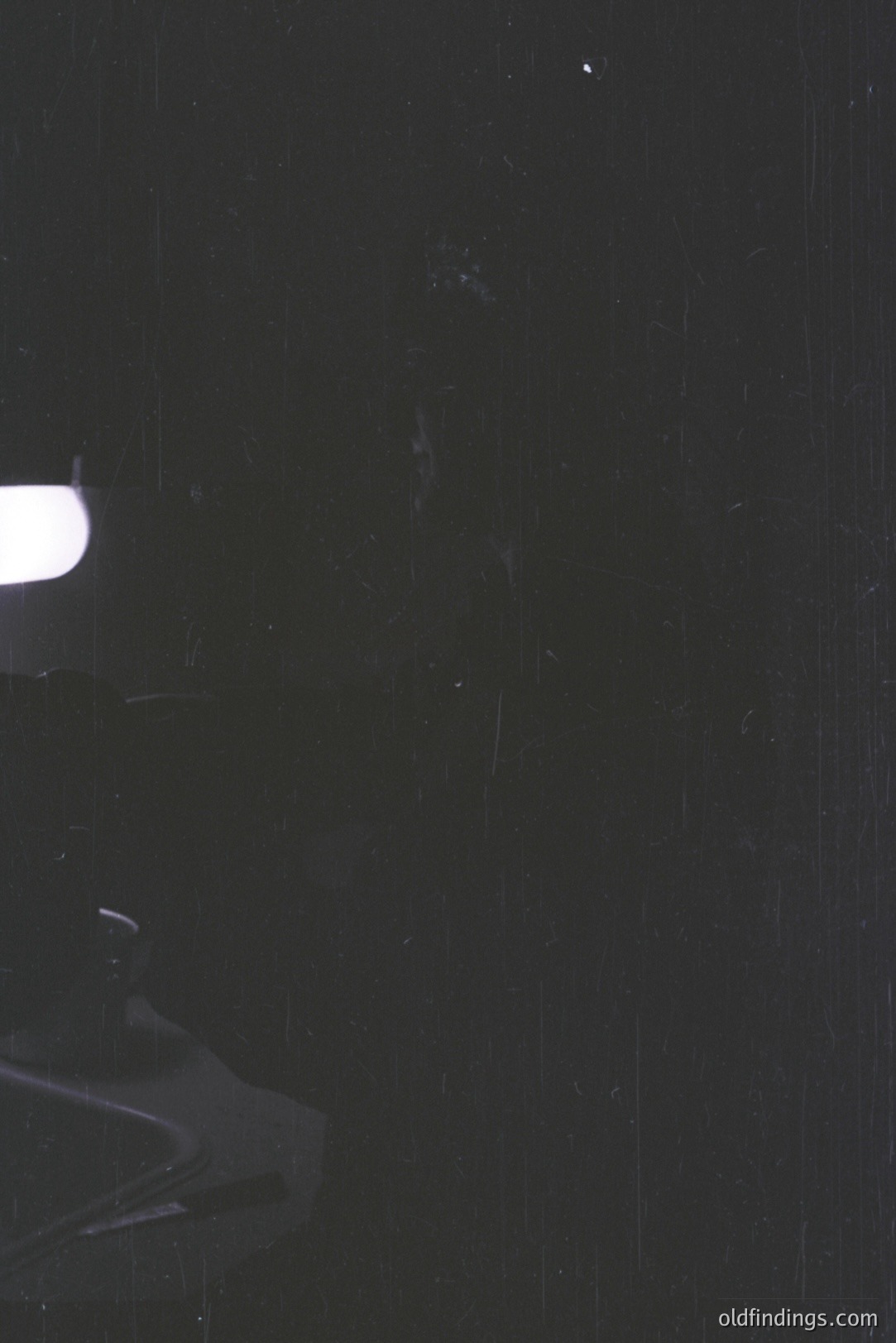 Black and white photograph featuring a partially visible vintage turntable. The record sits on the platter, illuminated by a bright studio light. Grainy texture and dust specks suggest age/archival nature. Likely 1970s-80s, reflecting analog recording era. Useful for retro design/music-themed projects.