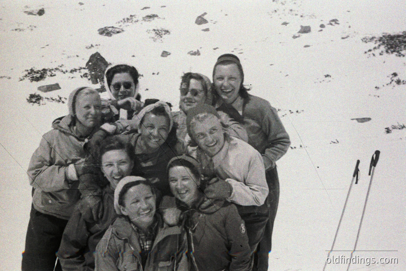 A group of women, bundled in warm outerwear, pose outdoors in a snowy landscape. Smiling faces, knit hats, and vintage ski equipment suggest a recreational outing. Likely 1960s-70s, emphasizing winter leisure and female camaraderie. A charming visual for historical context or design.