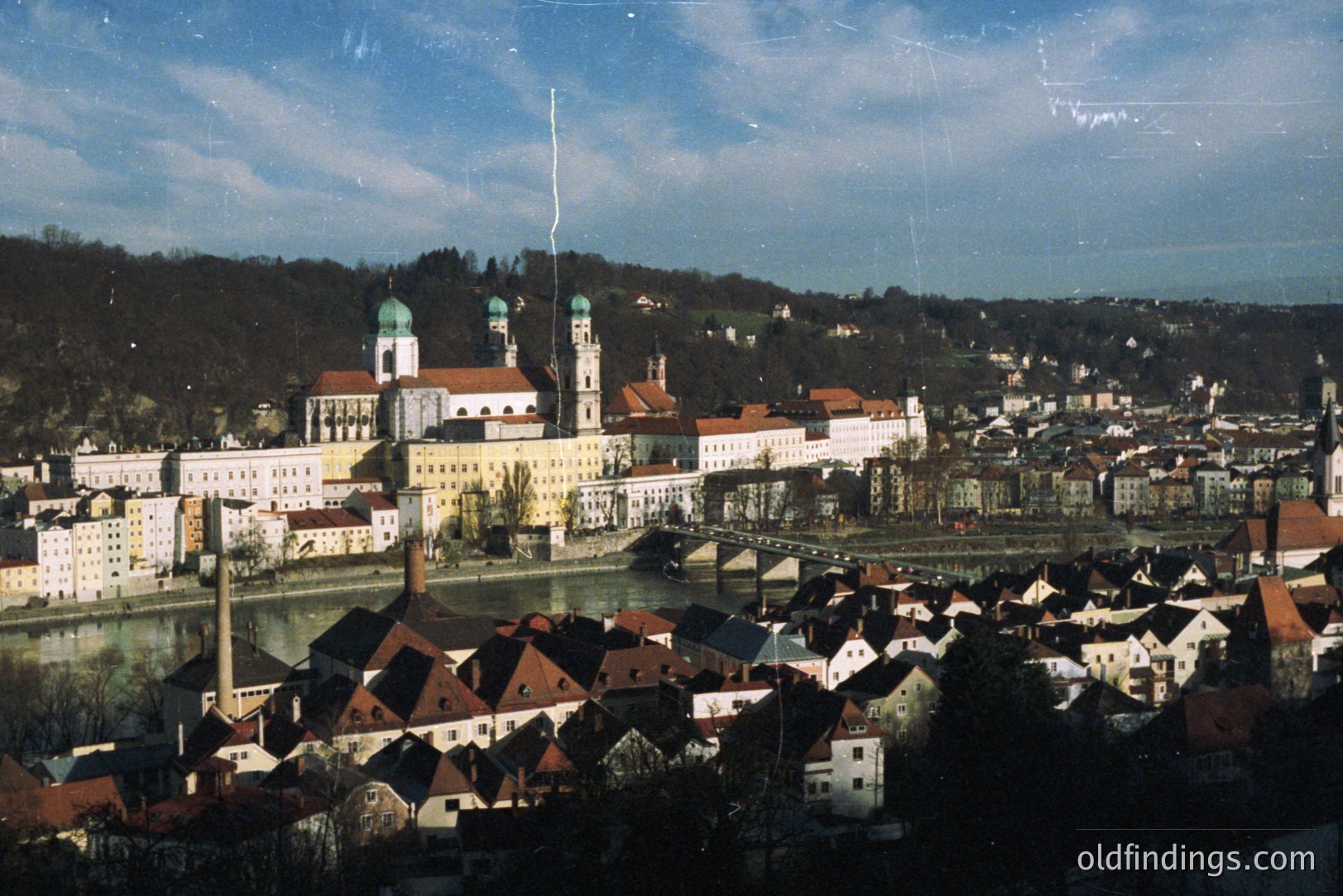 A panoramic view captures Passau, Germany. The Danube and Inn rivers converge, with the Dom St. Stephan, a Baroque cathedral, dominating the skyline. Traditional, tightly-packed townhouses with red-tiled roofs line the riverbanks. Appears to be a vintage travel photograph, possibly 1970s.