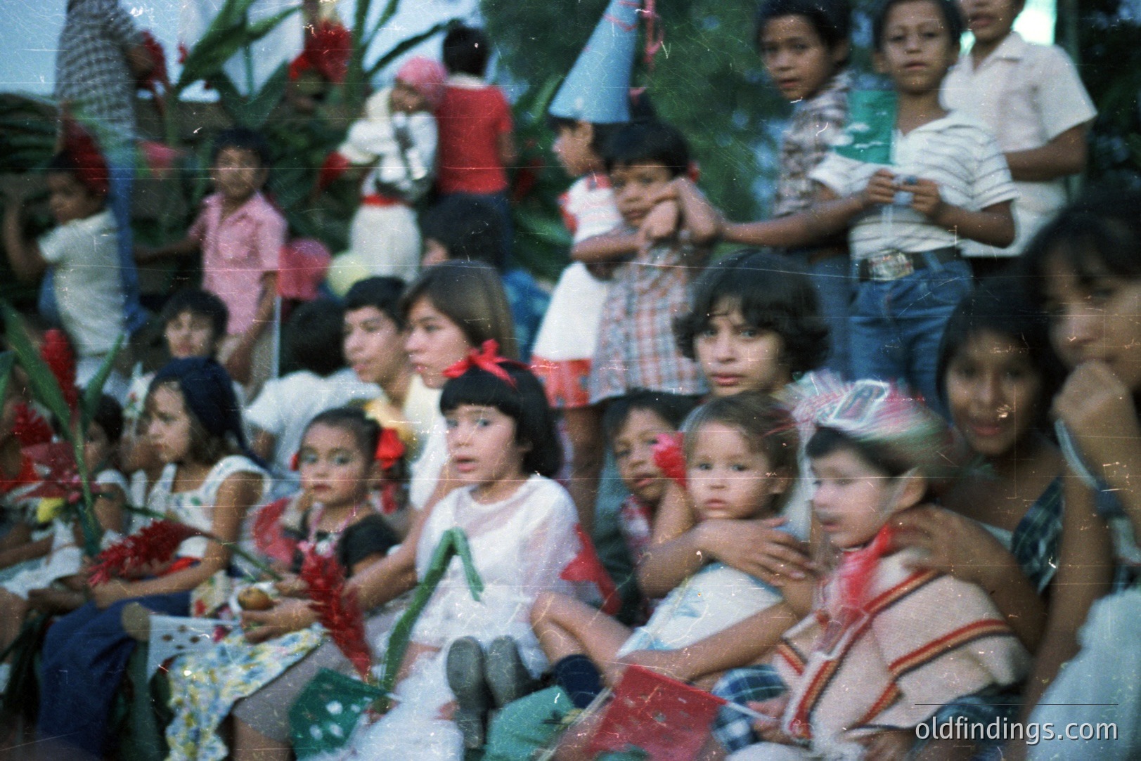 A candid moment captures a group of children, likely in a rural setting. They appear to be watching a procession or event; vibrant decorations are visible. Clothing styles suggest the 1970s. The color palette is characteristic of slide film from that era. A valuable resource for documenting childhood and community events.