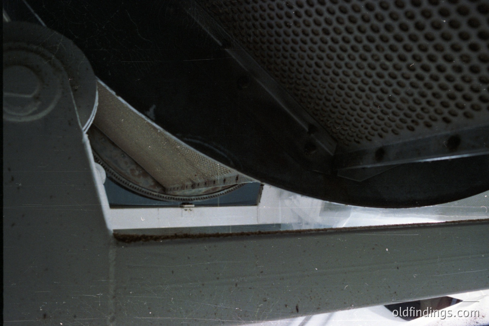 Industrial ventilation system detail showing a curved metal duct with perforated screen. Visible are structural supports and a glimpse of a white interior surface. Likely from a commercial or industrial building.