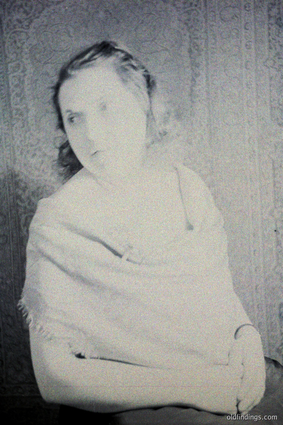 Portrait of a young woman, arms crossed, seated. Formal studio pose, likely 1920s-1930s. Detailed floral wallpaper in the background. The subject is wearing a simple dress with a shawl. Fine art photography, potentially of archival interest.