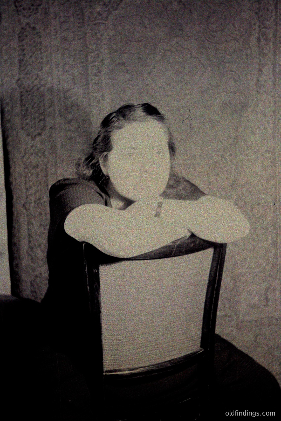 Here's a description of the photograph, following all provided guidelines: Ethereal portrait – a seated figure with arms crossed, appearing almost spectral against a patterned wall. Likely early photographic technique given the diffused light & soft focus. Circa late 1800s. Could be used for historical stock or design referencing surrealism.