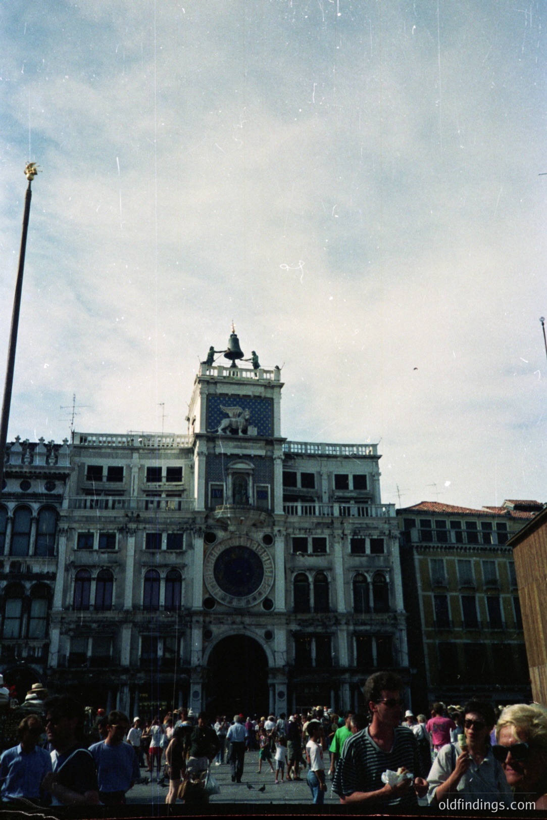 Palazzo Doge, Venice, Italy. A crowd gathers on the Piazzetta San Marco, framed by the basilica and this iconic Venetian palace. Note the ornate facade, the winged lion of Saint Mark, and the elevated viewing platform. Likely 1980s-90s film photography. Excellent for travel design.