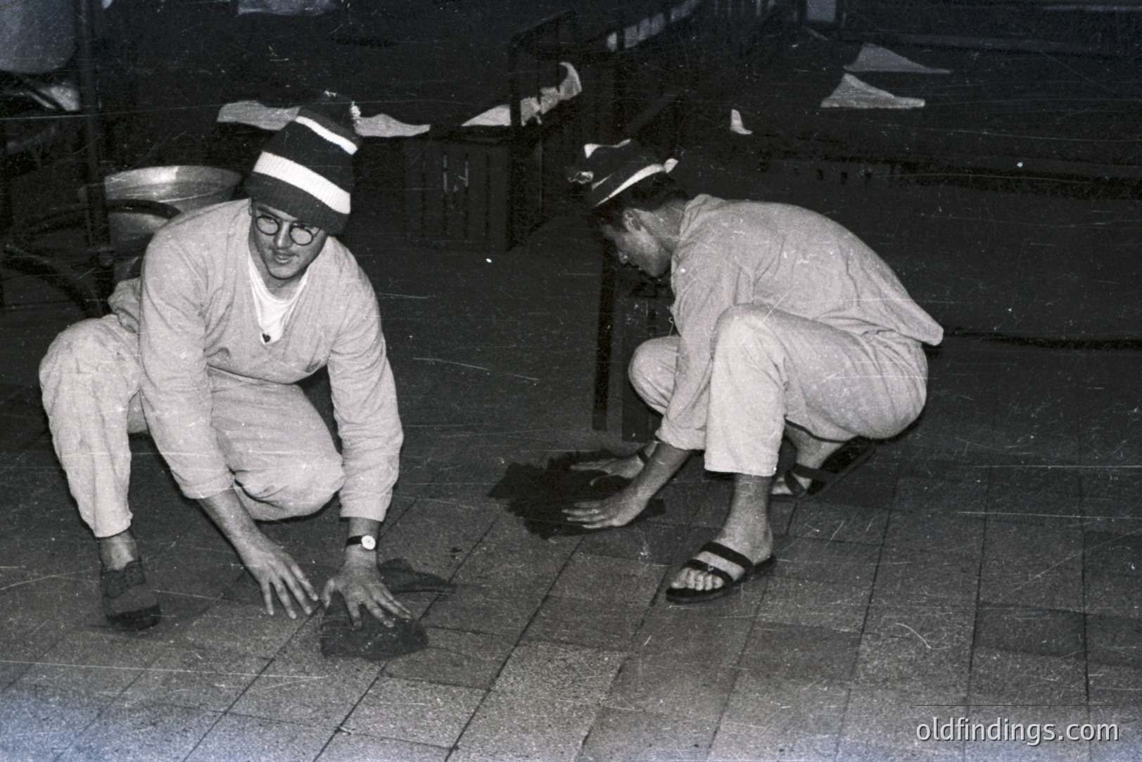 Two men in what appears to be hospital attire and caps kneel, examining a dark object on a tiled surface. Likely a medical or research setting, possibly involving a lab animal or specimen. Distinctive 1960s/70s style. The image has scientific/historical research potential.