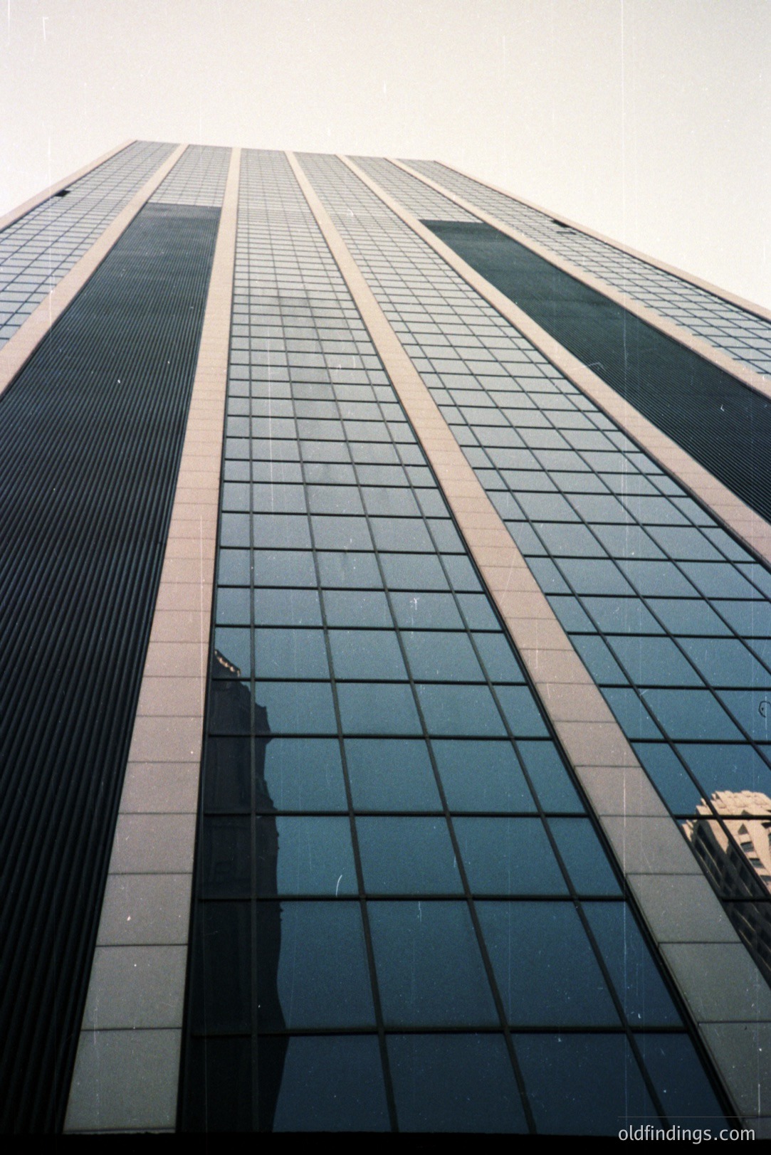 Striking upward view of a modern skyscraper with a grid of reflective windows and prominent horizontal architectural details. Appears to be a 1970s or 80s design; could be located in a large urban center. Excellent for architectural stock or design references.