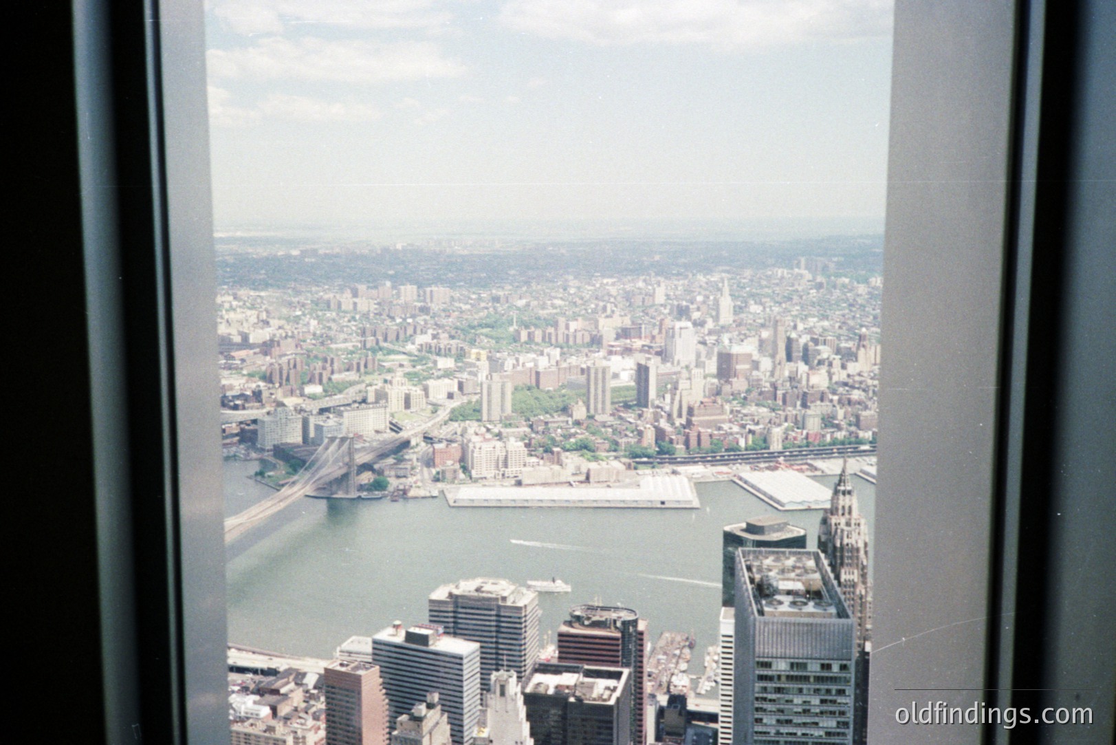 A high-angle view from a skyscraper showcases a dense urban landscape dominated by the East River and a bridge (likely the Manhattan Bridge). Detailed architecture reveals a mid-20th century aesthetic. Likely taken in the 1960s-1970s, this scene offers a glimpse of New York City's urban evolution.