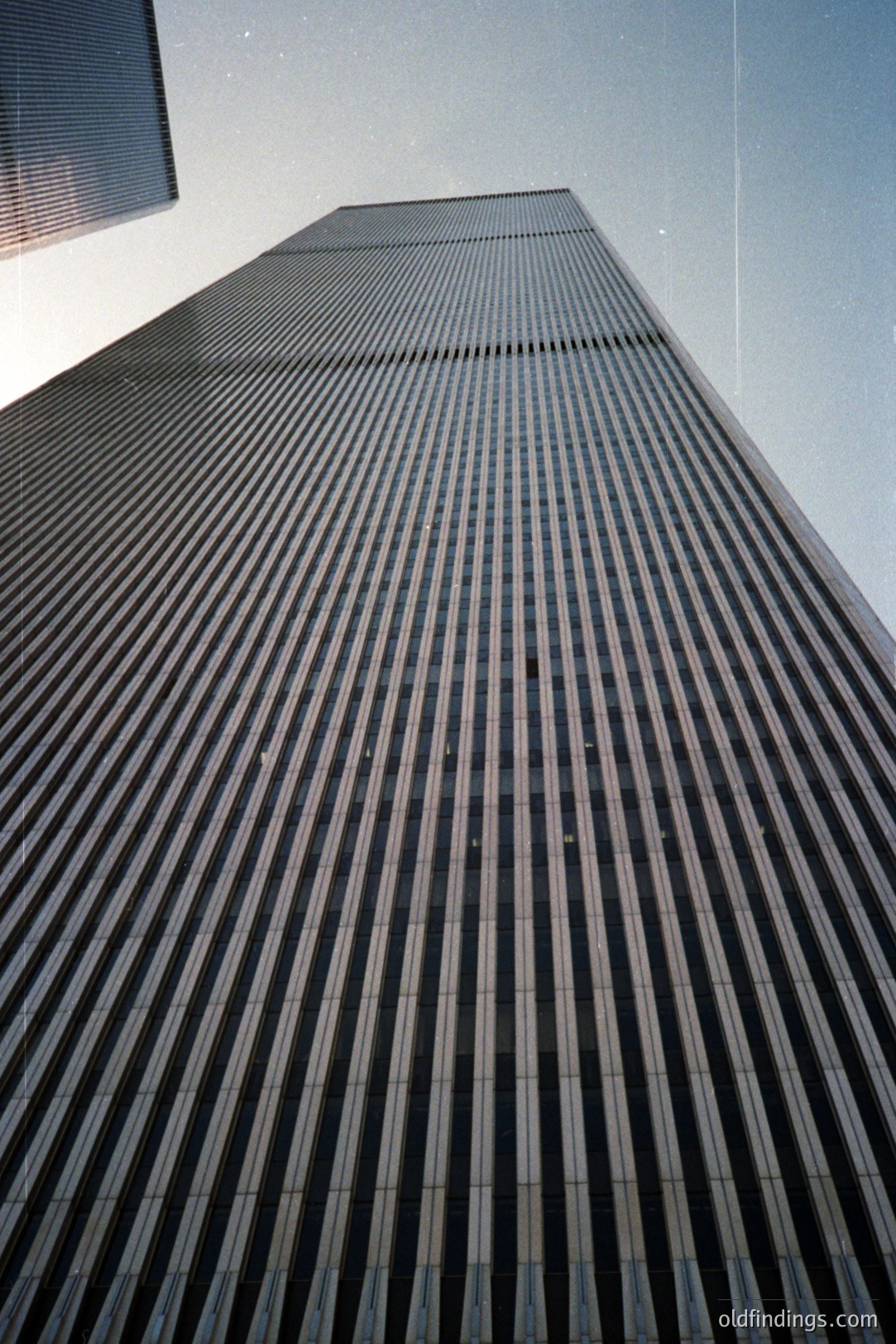 Striking low-angle view of a tall, modernist skyscraper, its facade defined by a grid of vertical and horizontal dark lines. Appears to be a pre-digital photograph, evidenced by dust and light leaks. Likely a 1970s or 80s architectural study.