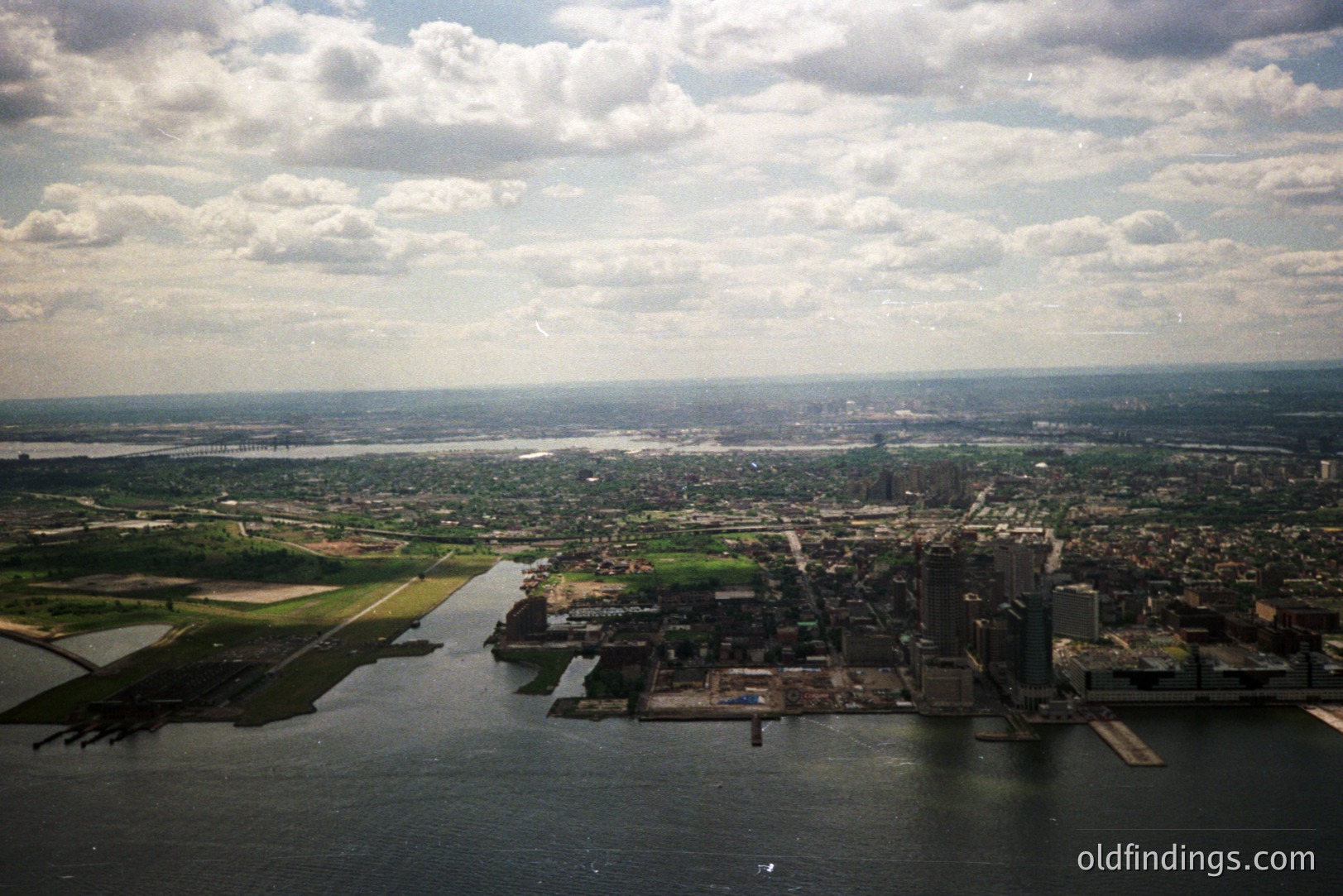 Aerial view of Montreal, Canada, showcasing the St. Lawrence River and cityscape. Prominent skyscrapers define the downtown area, while green spaces and waterways extend toward the horizon. Likely taken in the 1970s or 80s given the architectural styles and film quality. Relevant for urban planning & design studies.