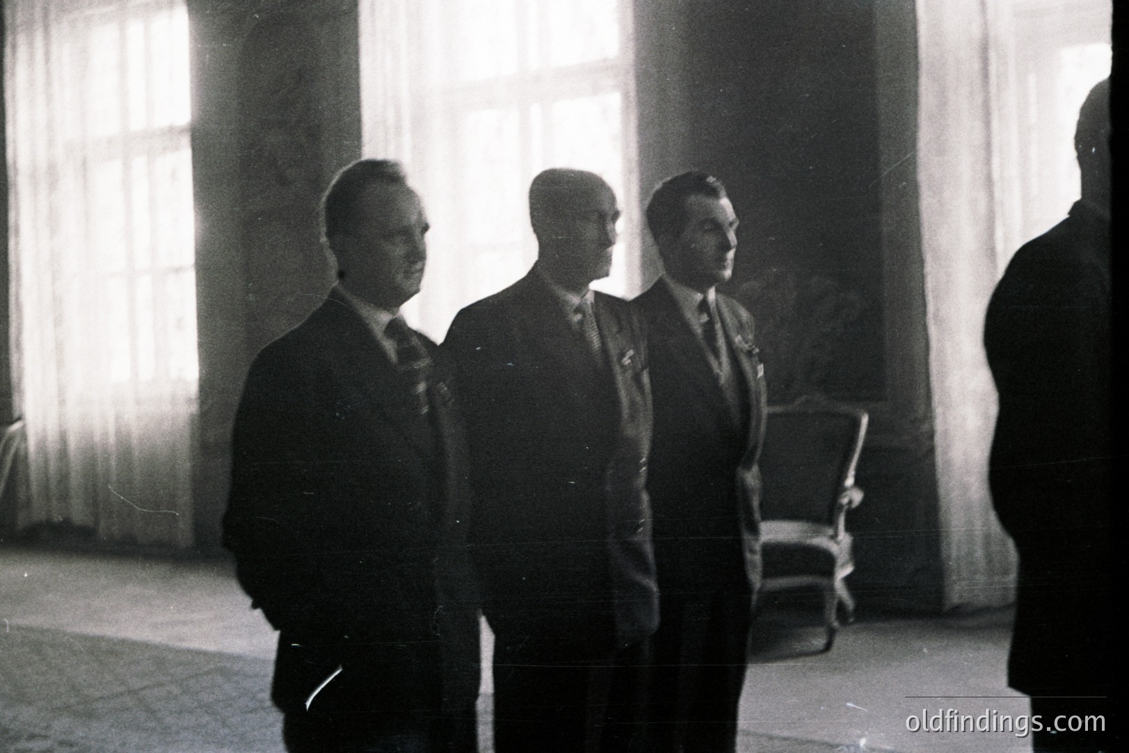 Three formally dressed men stand in a spacious, light-filled room with sheer curtains. The image appears to be a candid moment, likely a meeting or event. Architectural details suggest a historic building. Likely mid-20th century, possibly 1950s-1970s.