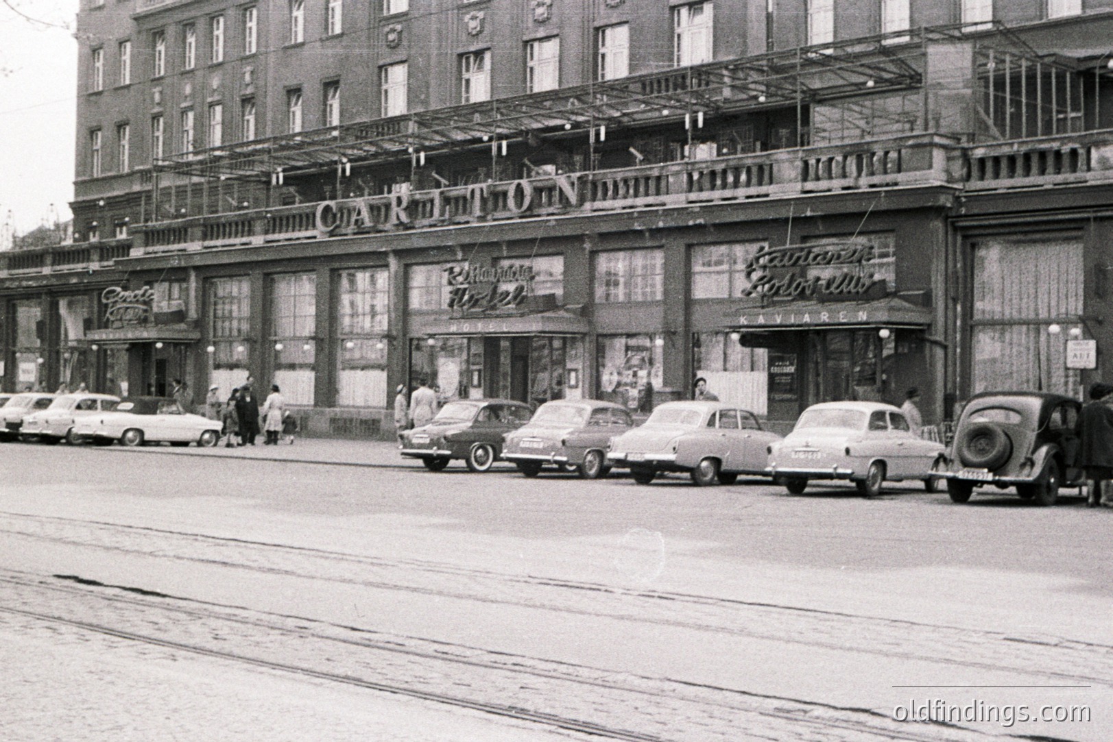 Exterior view of the Carlton Hotel & Casino in Varna, Bulgaria, circa 1960s. Shows a wide, imposing facade with a prominent awning and large windows. Several vintage cars are parked along the street. Pedestrians approach the entrance. Likely a valuable archive image for travel and casino history.