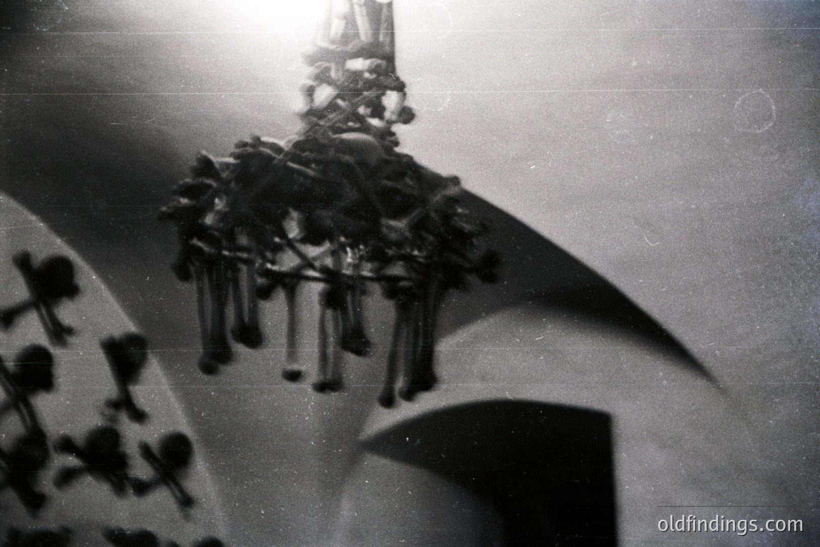 A dramatic, high-angle view captures a multi-tiered chandelier suspended within an arched interior space. The architecture features curved ceilings and suggests a monumental scale. Grainy black and white aesthetic hints at a mid-20th century (1960s-1970s) photographic style. Likely an architectural detail or interior design reference.