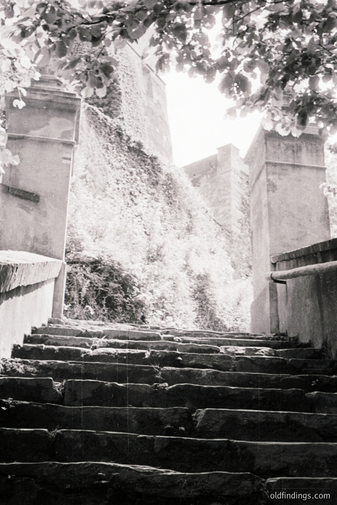 Stone steps ascend towards a bright, overexposed opening framed by weathered architecture and foliage. The textured surfaces suggest a historical location, possibly a coastal town. The composition highlights the interplay of light and shadow on the stone. Likely dating from mid-20th century.