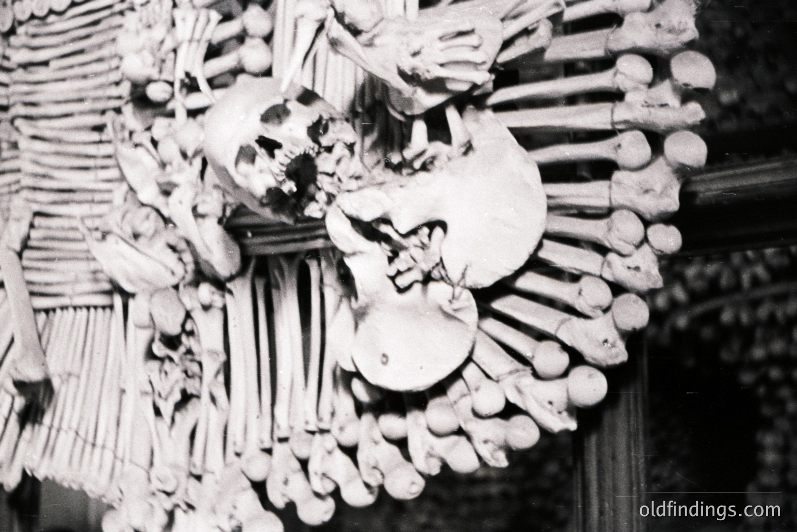 A macabre decorative piece, likely a wall hanging, constructed from animal bones and a human skull. The arrangement features numerous vertebrae, ribs, and long bones radiating outwards, creating a radial pattern. Appears to be a folk art or ceremonial object. Likely mid-20th century.